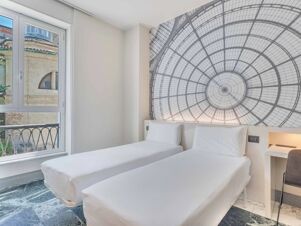 Two single beds with white linens next to a large window and a wall mural in a room at B&B Hotel Milano Sant'Ambrogio