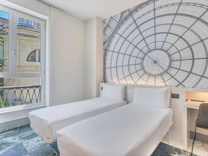 Two single beds with white linens next to a large window and a wall mural in a room at B&B Hotel Milano Sant'Ambrogio