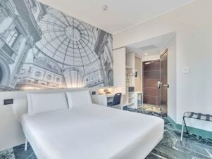 Hotel room at B&B Hotel Milano Sant'Ambrogio featuring a large bed, desk with chair, wardrobe, and wall mural of a glass domed ceiling