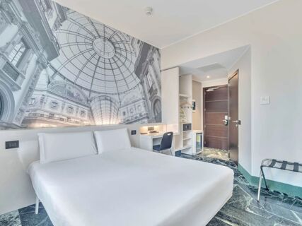 Hotel room at B&B Hotel Milano Sant'Ambrogio featuring a large bed, desk with chair, wardrobe, and wall mural of a glass domed ceiling