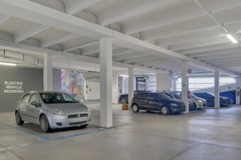 Indoor parking area at B&B Hotel Milano Sesto Marelli with white concrete beams and cars, electric vehicle reserved space visible