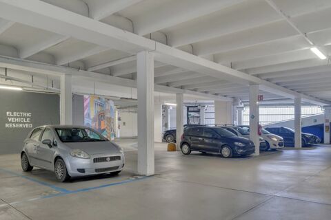Indoor parking area at B&B Hotel Milano Sesto Marelli with white concrete beams and cars, electric vehicle reserved space visible