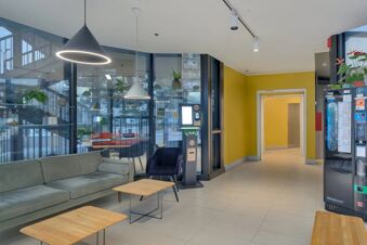 Modern hotel lobby with gray sofa, blue chair, hanging lights, glass walls, and vending machines at B&B Hotel Milano Sesto Marelli