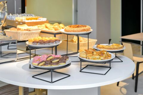 Various pastries, muffins, donuts, croissants, and breads displayed on stands and baskets in B&B Hotel Milano Sesto Marelli