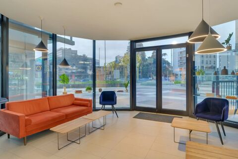 Interior of B&B Hotel Milano Sesto Marelli lobby with orange sofa, blue chairs, wooden tables, hanging lights, and large glass windows