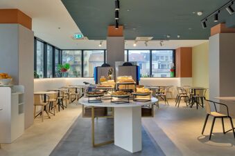 Modern breakfast area at B&B Hotel Milano Sesto Marelli with round table displaying assorted pastries and stocked beverage dispensers