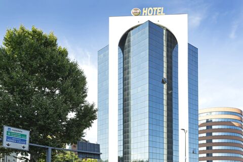 Tall modern building with reflective glass windows and a large B&B Hotel Milano Sesto Marelli sign on top against a blue sky