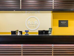 Reception desk with Lenovo computers and a yellow wall featuring a B&B Hotels logo and reception sign at B&B Hotel Fabriano Janus