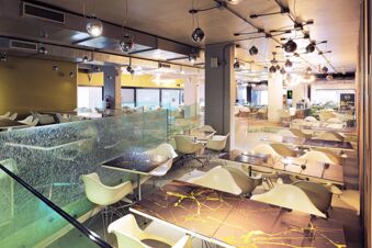 Dining area with modern white chairs, tables with marble patterns, spherical hanging lights, and glass partitions at B&B Hotel Fabriano Janus