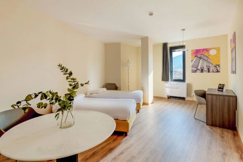 Minimalist hotel room at B&B Hotel Fabriano Janus with two single beds, wooden floor, window, desk, and a round table with plant