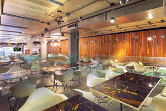 Interior view of a spacious dining area with white chairs, dark marble tables, glass partitions, and wooden walls at B&B Hotel Fabriano Janus