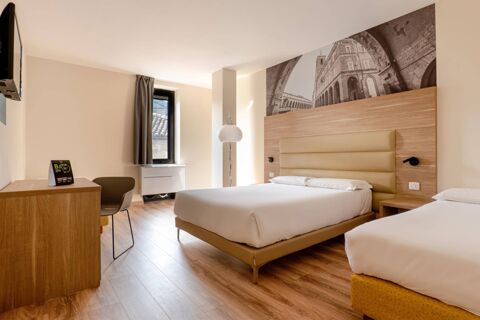 Hotel room at B&B Hotel Fabriano Janus with two beds, wooden headboards, a desk with chair, and a wall-mounted TV