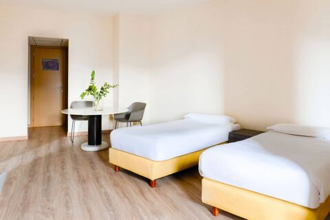 Two single beds with white linens beside a round table with green plants and two gray chairs in B&B Hotel Fabriano Janus room