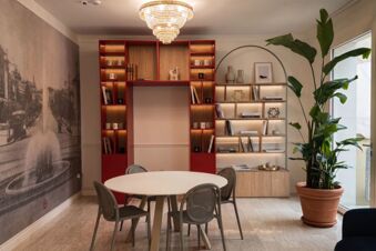 Round white table with gray chairs, red and wooden shelves, chandelier, and large potted plant in B&B Hotel Pesaro Des Bains