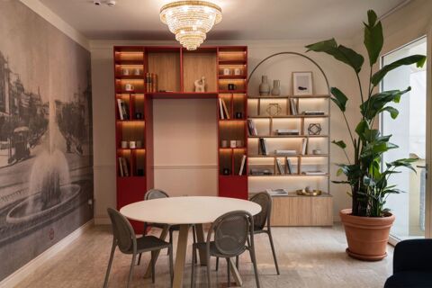 Round white table with gray chairs, red and wooden shelves, chandelier, and large potted plant in B&B Hotel Pesaro Des Bains