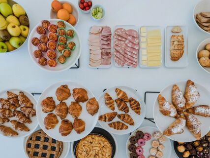 Assorted sliced meats, cheeses, bread, muffins, croissants, fruits, desserts, and vegetables displayed on plates at B&B Hotel Pesaro Des Bains