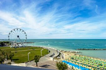 Coastal view from B&B Hotel Pesaro Des Bains showing a Ferris wheel, a beach with umbrellas, and the sea under blue sky