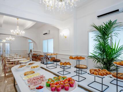 Buffet table with muffins, croissants, cold cuts, cheeses, bread, pastries, and a dining area at B&B Hotel Pesaro Des Bains