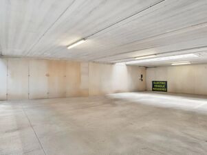 Empty concrete parking garage interior with overhead lights and a sign marking electric vehicle reserved space at B&B Hotel Torino Orbassano