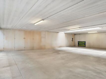 Empty concrete parking garage interior with overhead lights and a sign marking electric vehicle reserved space at B&B Hotel Torino Orbassano