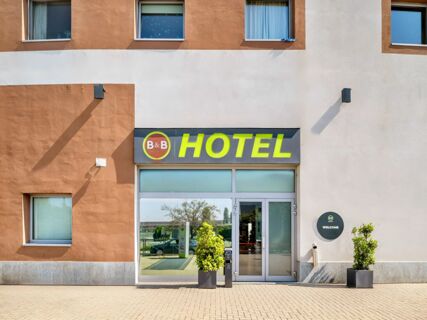 Entrance of B&B Hotel Torino Orbassano with glass doors, two potted plants, a large hotel sign, and an orange and white building facade