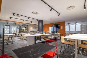 Modern dining area at B&B Hotel Sassari with white tables, wooden chairs, red metal chairs, and a buffet counter with appliances