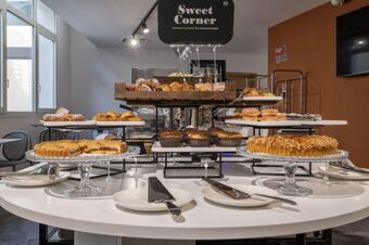 Various pastries and baked goods displayed on white plates and wooden trays at the Sweet Corner in B&B Hotel Sassari