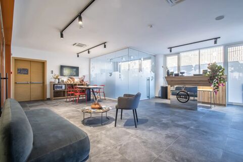 Spacious hotel lobby at B&B Hotel Sassari with seating area, wooden reception desk, glass meeting room, and red chairs around a table
