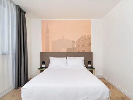 Double bed with white linens against a headboard featuring a cityscape mural, flanked by black wall lamps and small tables at B&B Hotel Catania Bellini