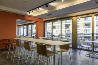 Dining area with long tables, wooden chairs, floor-to-ceiling windows, and a balcony at B&B Hotel Catania City Center