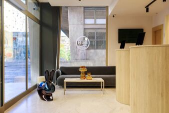 Modern hotel lobby interior with a curved wooden reception desk, dark sofa, marble table, and decorative vases at B&B Hotel Catania City Center