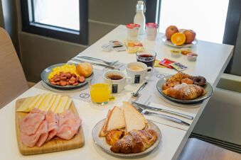 Breakfast spread on a white table including sliced ham, cheese, croissants, coffee, juice, fruit, and eggs at B&B Hotel Pisa Airport