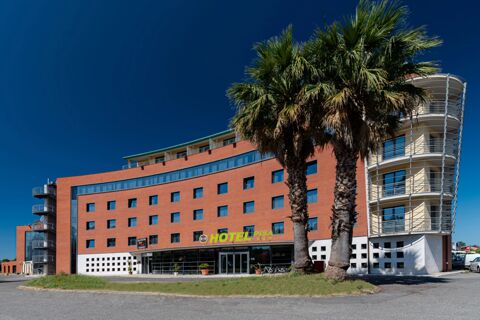 Large brick and glass building with balconies and palm trees in front showing B&B Hotel Pisa Airport on a clear blue sky day