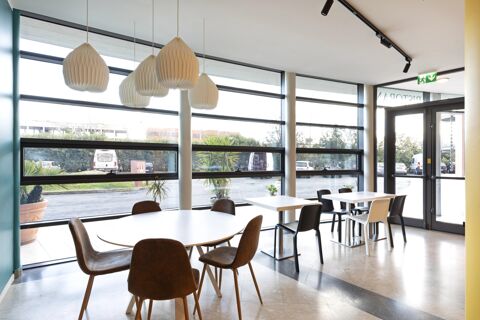 Bright dining area with pendant lights, round and square tables, chairs, large windows, and an exit door at B&B Hotel Pisa Airport
