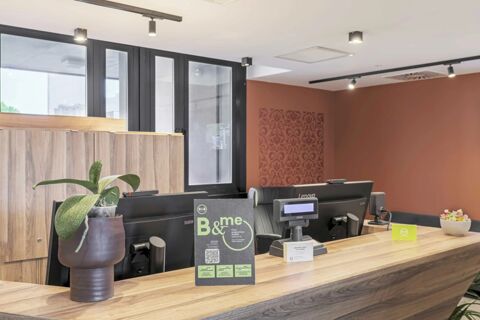 Reception desk area with computer monitors, potted plant, promotional sign, and cardholder at B&B Hotel Prato City Center