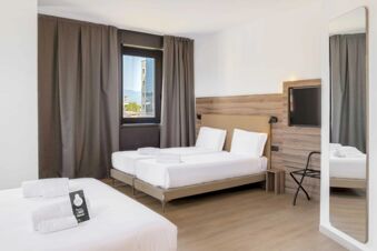Two neatly made beds with white linens and towels are in a modern hotel room at B&B Hotel Prato City Center with a window and mirror