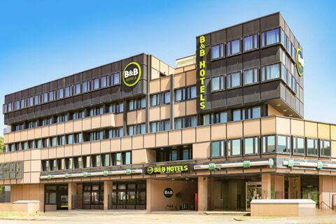 Modern multi-story building with beige and dark brown panels featuring B&B Hotel Prato City Center signage in yellow and green letters under a clear blue sky