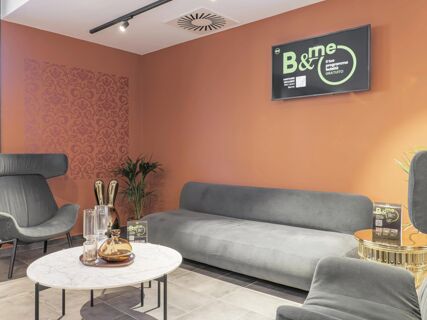 Modern lounge area with gray sofas, black armchairs, decorative vases on a marble table, and a TV screen at B&B Hotel Prato City Center