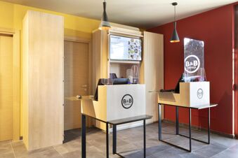 Reception area of B&B Hotel Bolzano featuring two wooden desks with glass protective screens and black pendant lights