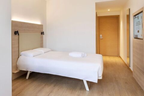 Single bed with white linens and two pillows, wooden headboard, wooden door, mirror, and a television screen in B&B Hotel Bolzano