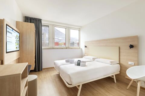 Twin beds with white linens and rolled towels in a bright room at B&B Hotel Bolzano featuring wooden furniture and a TV screen