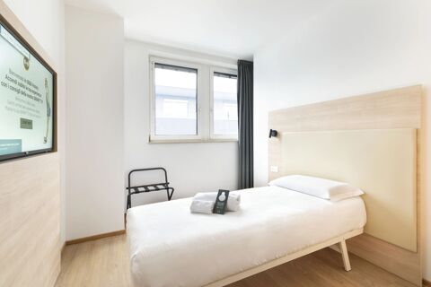 A single bed with white linens and a towel on top next to a window with dark curtains in a B&B Hotel Bolzano room