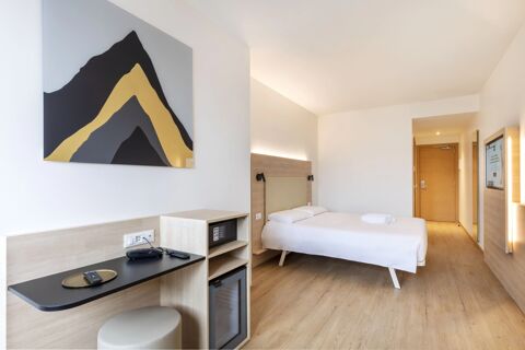 Minimalist hotel room at B&B Hotel Bolzano with a double bed, wood furniture, modern lighting, and abstract wall art
