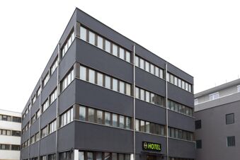 Dark gray multi-story building with rows of windows and a green B&B Hotel Bolzano sign near the entrance