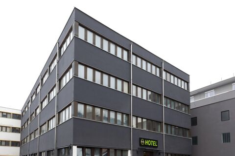 Dark gray multi-story building with rows of windows and a green B&B Hotel Bolzano sign near the entrance