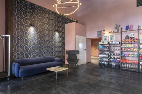 Modern seating area with a blue sofa and black armchair, geometric patterned wall, and shelves with snacks at B&B Hotel Passo Tre Croci Cortina
