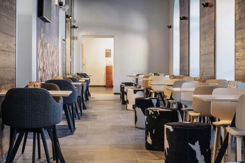 Dining area in B&B Hotel Passo Tre Croci Cortina with wooden walls, gray chairs, wooden tables, and cowhide stools along windows