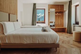 Two neatly made twin beds with white linens and folded towels in a room featuring wood accents and a mountain view window at B&B Hotel Passo Tre Croci Cortina