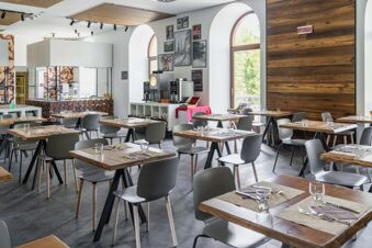Dining area with tables set with glasses and cutlery, serving counters, coffee machines, and arched windows at B&B Hotel Passo Tre Croci Cortina