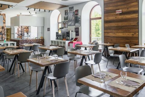 Dining area with tables set with glasses and cutlery, serving counters, coffee machines, and arched windows at B&B Hotel Passo Tre Croci Cortina